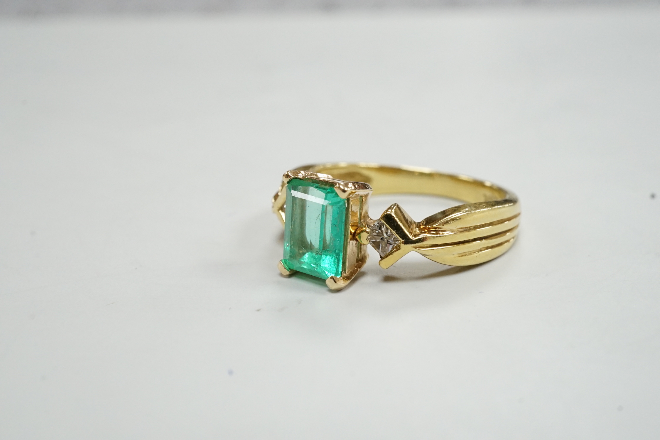 A modern 18k yellow metal and single stone emerald set ring, with two stone diamond set shoulders, size O, gross weight 5.8 grams.